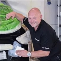 Roy utfører karosserireparasjon på bil med maskerte flater i moderne verkstedmiljø.